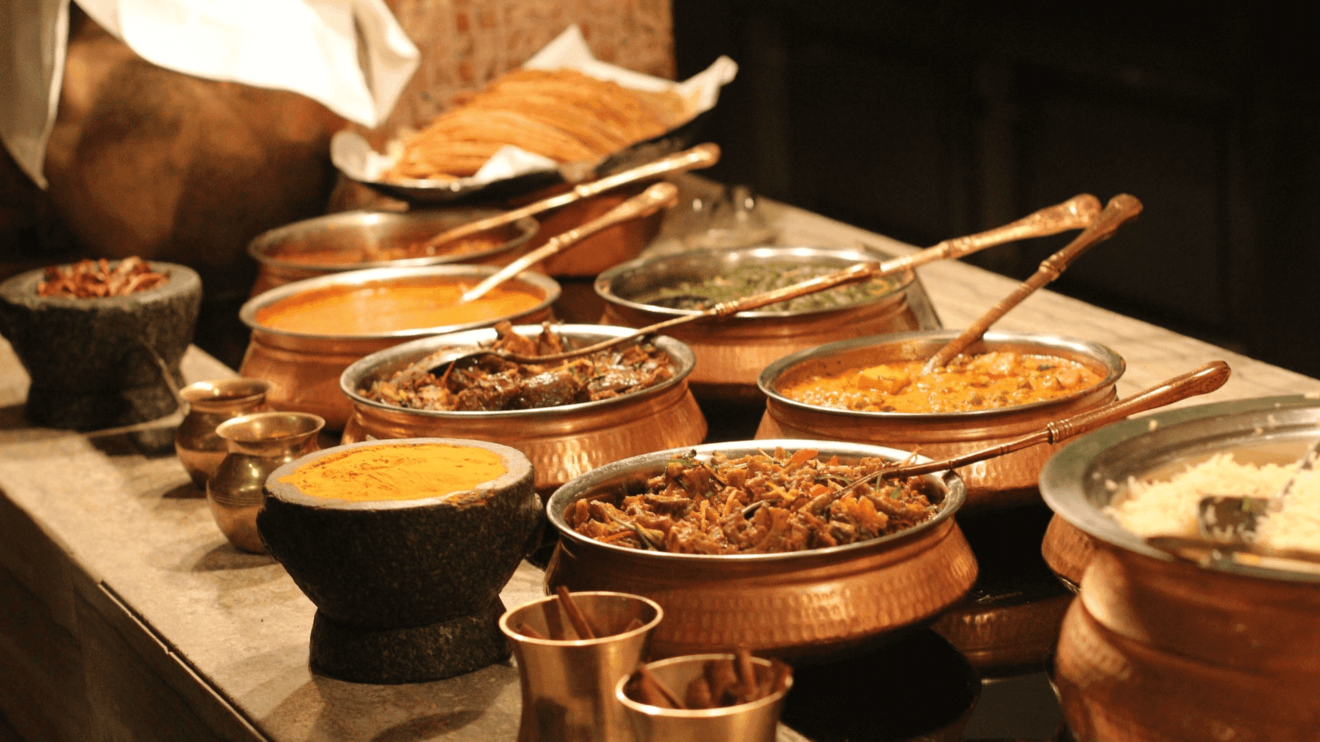An assortment of Indian dishes in copper pots on a buffet table, ready to be served.